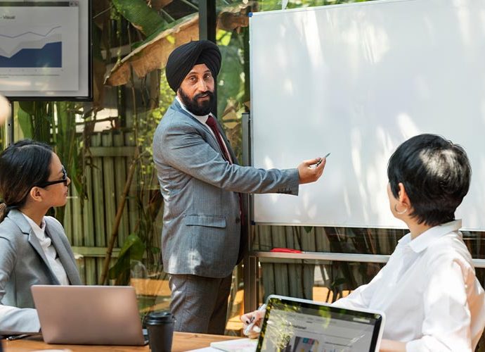 A man in a turban presenting to colleagues in a professional setting.