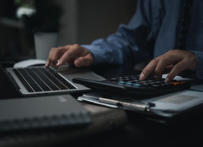 A person working on financial calculations and data analysis using a calculator and laptop on a desk.